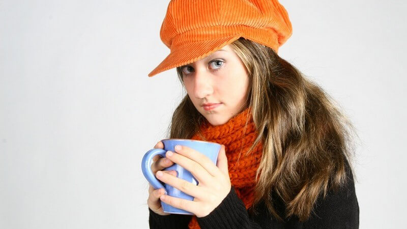 Mädchen mit blauer Tasse in den Händen, orangener Mütze und Schal