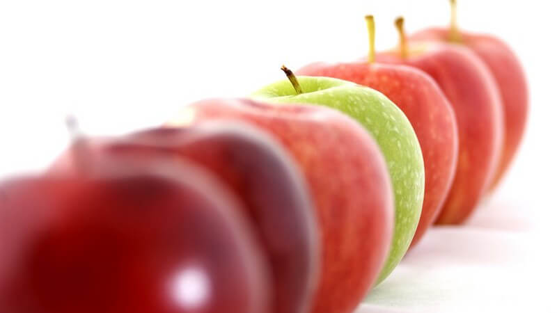 Rote Äpfel und ein grüner in einer Reihe auf weißem Hintergrund