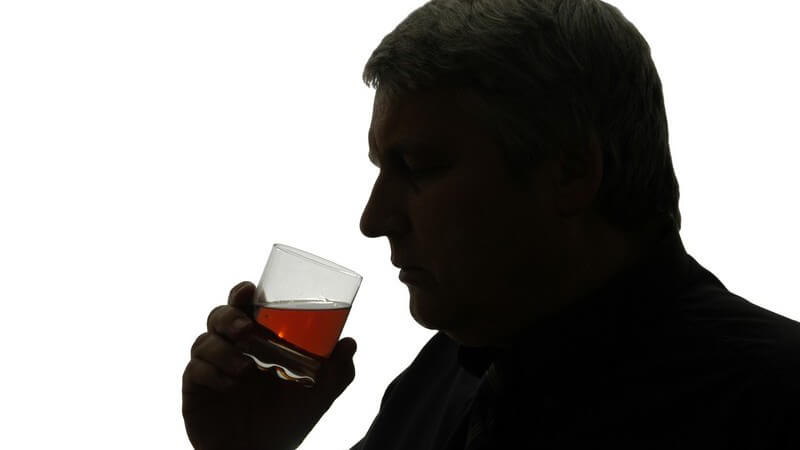Dunkler Mann trinkt alkoholisches Getränk aus einem Glas vor weißem Hintergrund