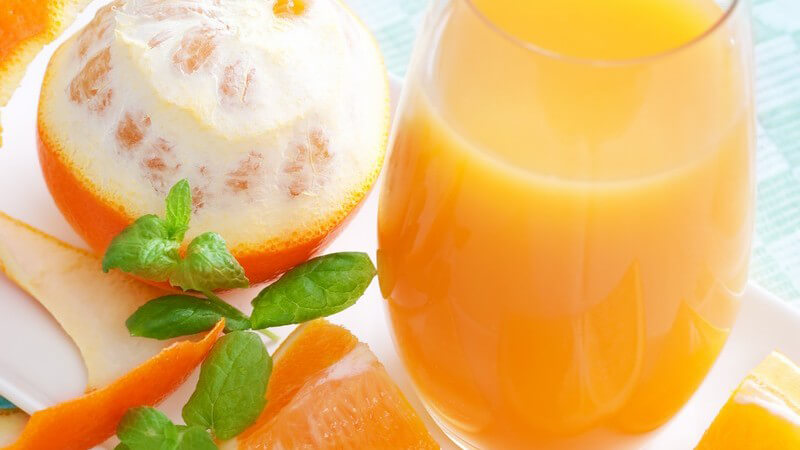 Glas mit frisch gepresstem Orangensaft, daneben frische Orange