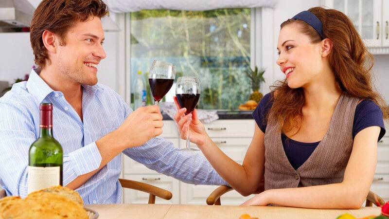 Junges Paar sitzt am Küchentisch und stößt mit Rotwein an