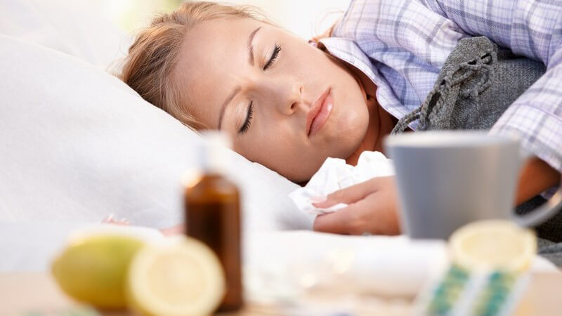 Junge Frau mit Erkältung schläft im Bett, vor ihr Medikamente