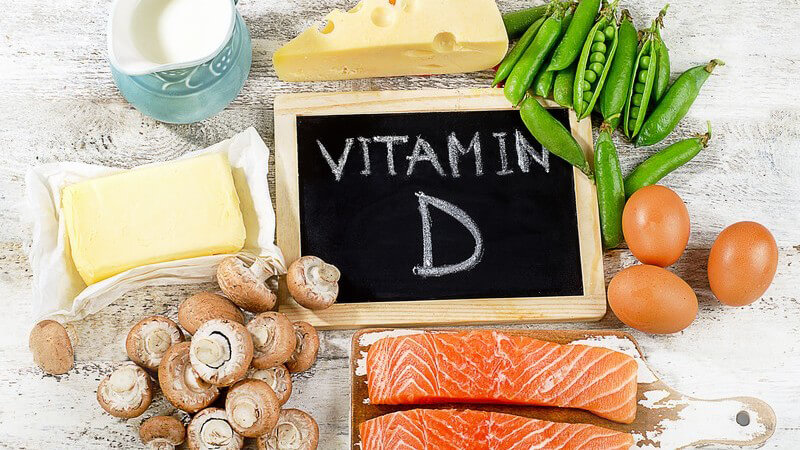Vitamin D-haltige Nahrungsmittel wie Lachs, Champignons, Butter, Käse, Erbsen und Eier, mit Beschriftung auf Tafel