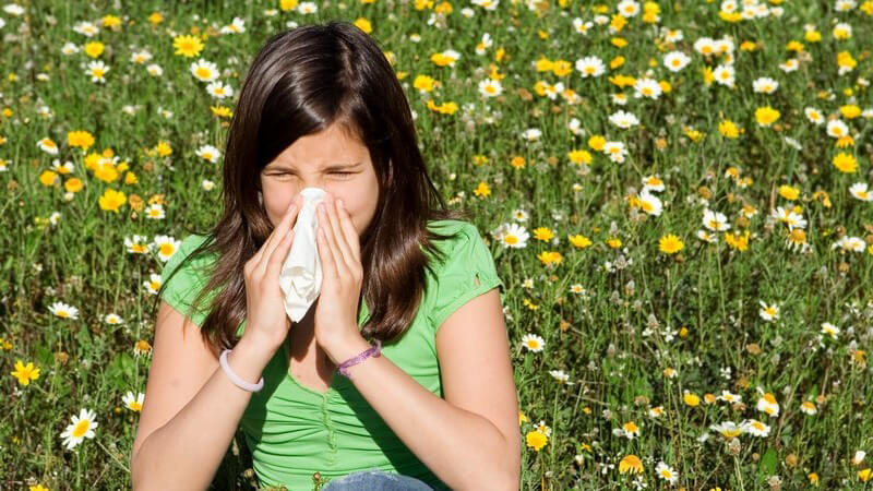 Mädchen auf Blumenwiese putzt sich die Nase, allergisch