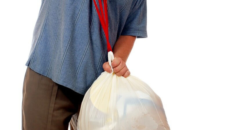 Mann zieht vollen Müllbeutel aus Mülleimer