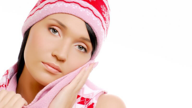 Junge, dunkelhaarige Frau mit rosa Mütze und Schal, schmiegt sich an den Schal