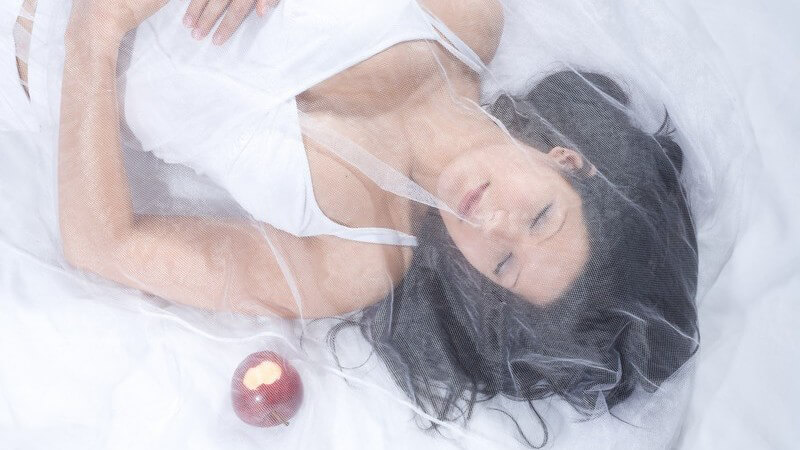 Dunkelhaarige Frau liegt unter Schleier und schläft, daneben roter Apfel, Schneewittchen