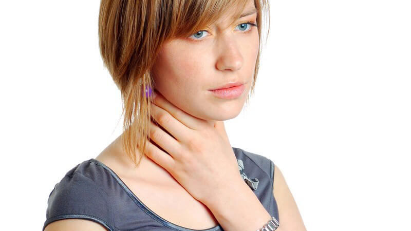 Junge Frau mit Halsschmerzen fasst sich an den Hals, weißer Hintergrund