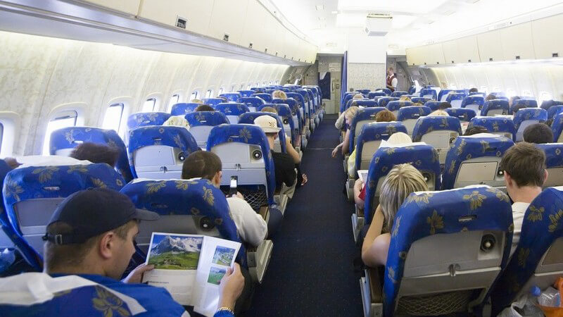 Rückansicht Gang im Innenraum eines Flugzeuges, mehrere Menschen in Sitzreihen