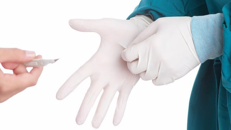 Chirurg zieht Handschuhe an, ihm wird ein Skalpell gereicht