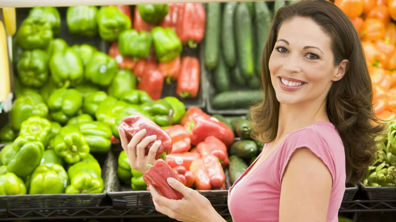 Junge Frau im Supermarkt hält Paprika in Händen