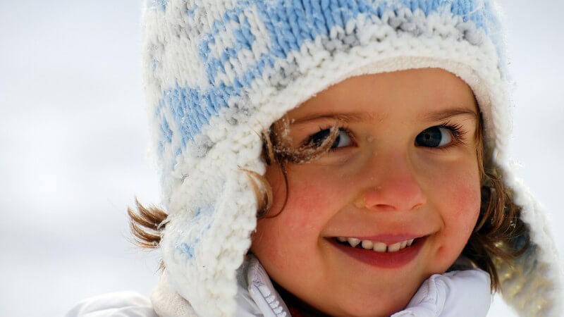 Kleines Mädchen mit Wollmütze lacht in Kamera