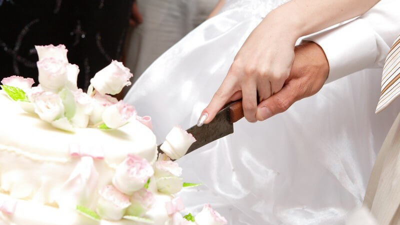 Weiße Hochzeitstorte wird von Brautpaar gemeinsam angeschnitten