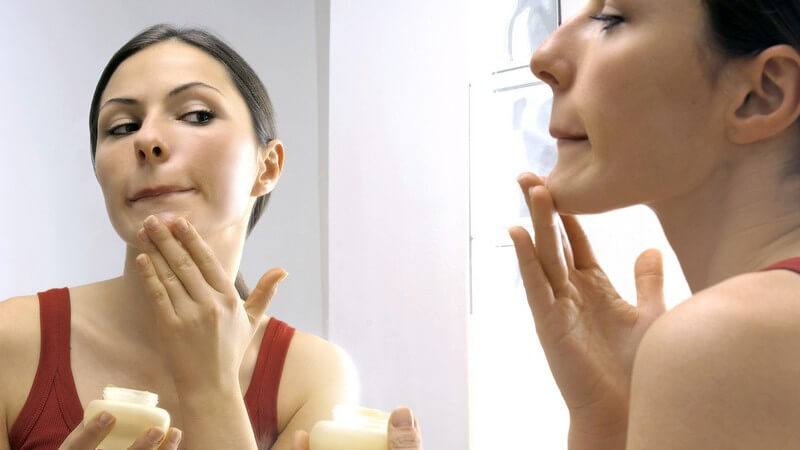 Junge Frau vor Spiegel trägt Gesichtscreme auf