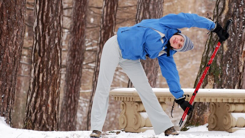 Frau in blauer Trainingsjacke wärmt sich mit Nordic Walking Stöcken auf