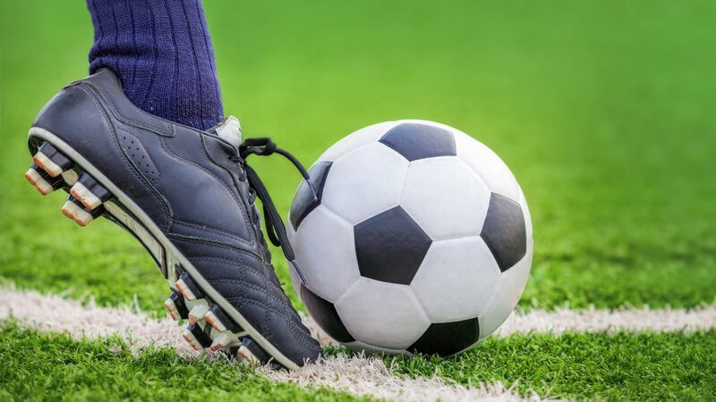 Fuß mit dunkelblauem Stutzen und schwarzem Fußballschuh schießt einen Fußball mit dem Vollspann