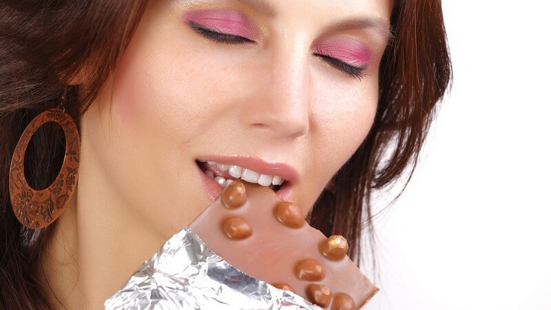 Junge Frau genießt Biss in Tafel Schokolade, weißer Hintergrund