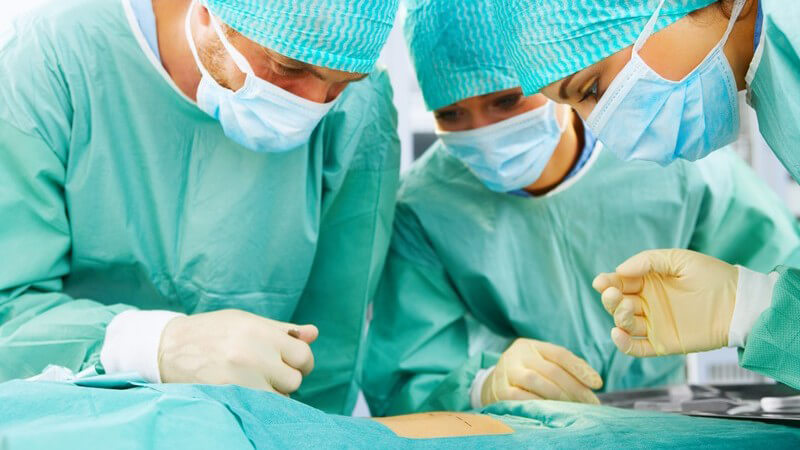 Drei Chirurgen mit grünen Kitteln und Mundschutz bei Operation