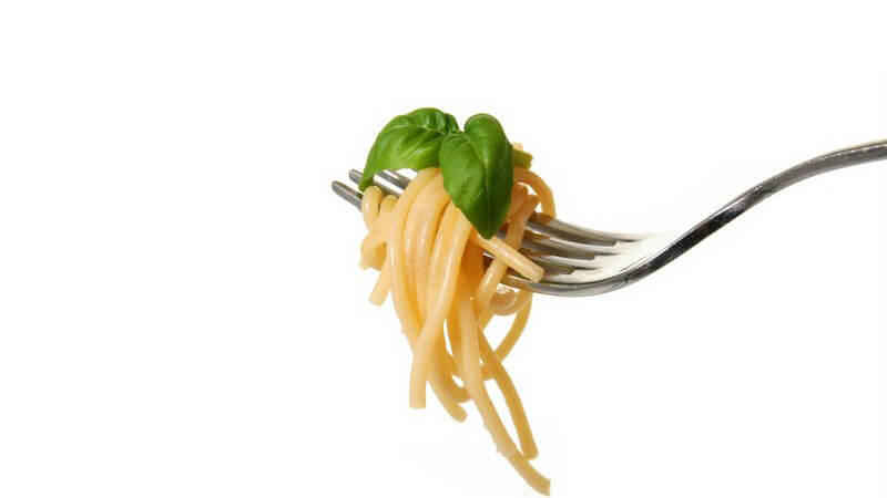 Gabel mit aufgerollten Spaghetti, garniert mit frischem Basilikum