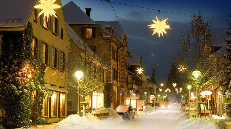 Beleuchtete Straße mit Weihnachtssternen und Schnee auf der Straße