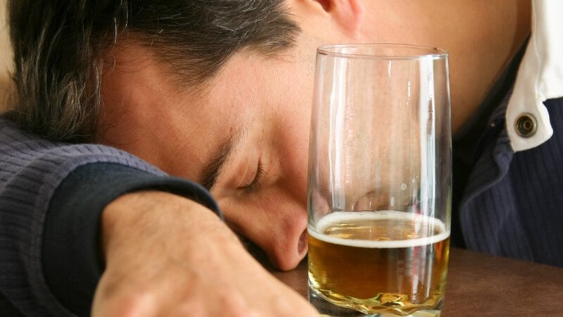 Junger Mann hat Kopf auf Arm auf Tisch aufgestützt und schläft, daneben fast leeres Bierglas