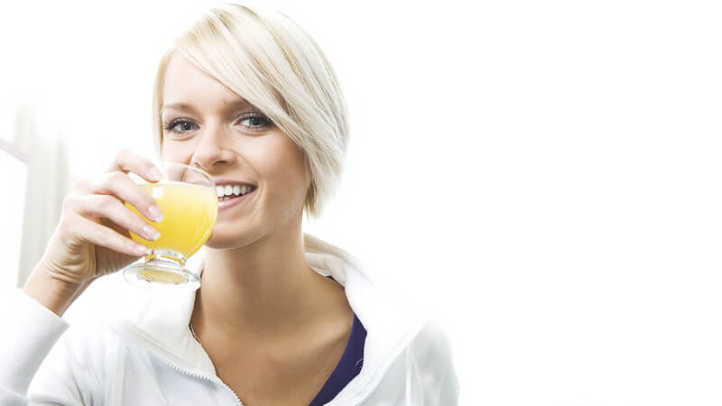 Junge blonde Frau trinkt Fruchtsaftgetränk, neben ihr liegen helle Trauben