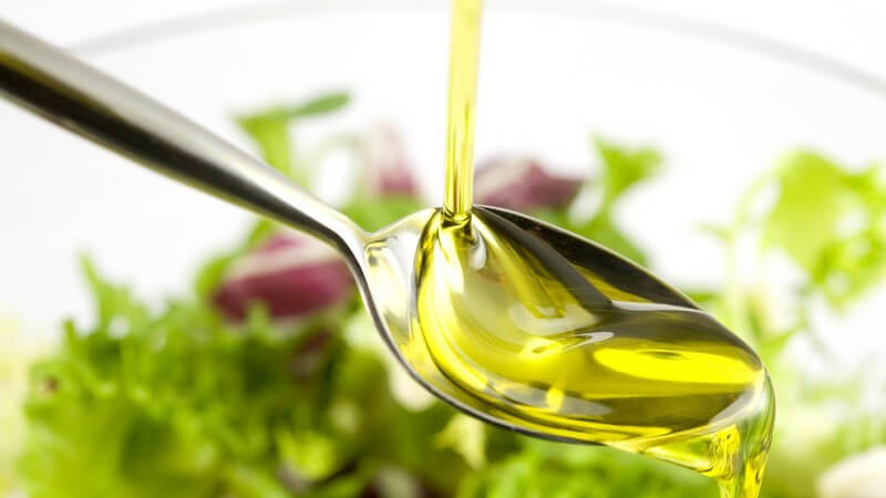 Nahaufnahme Öl wird auf Löffel gegossen, darunter Salat