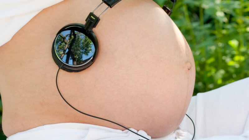Kopfhörer auf nacktem schwangerem Bauch