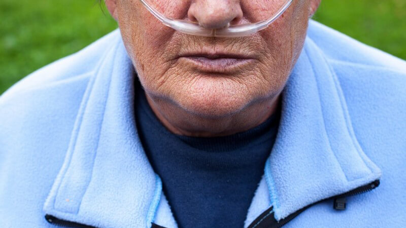 Lungenkranke Seniorin in hellblauer Fleecejacke mit Sauerstoffschlauch in der Nase