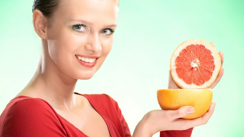 Blonde lächelnde Frau hält halbierte Grapefruit in Kamera