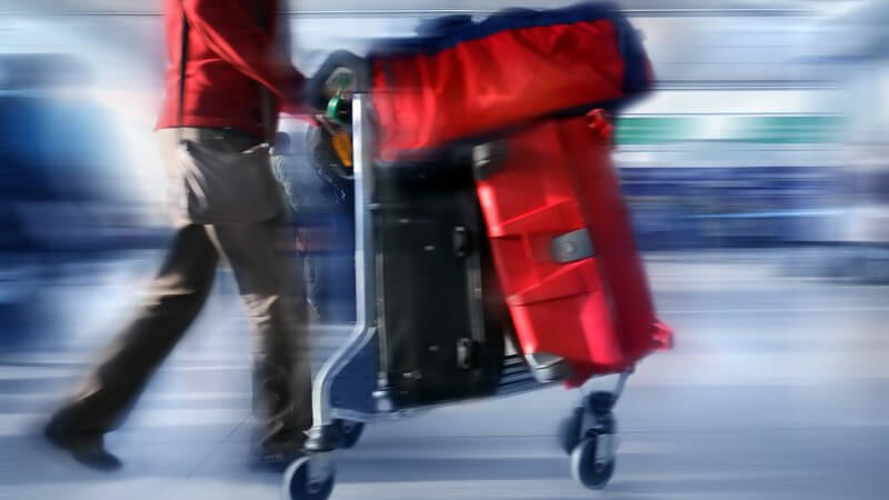 Mann schiebt Gepäckwagen mit roten Koffern