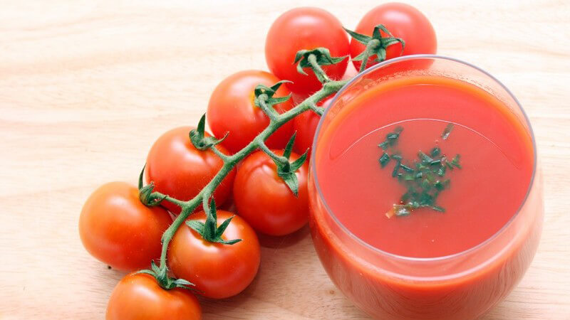 Glas Tomatensaft mit Kräutern von oben fotografiert, daneben ein Zweig Tomaten