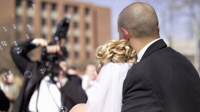 Hochzeitspaar von hinten gesehen, vor ihnen ein Fotograf und Seifenblasen