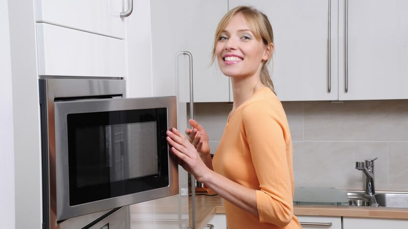 Frau in moderner Küche steht vor Mikrowelle