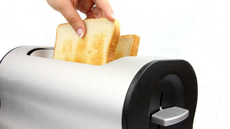 Frauenhand holt zwei fertige Toasts aus dem Toaster
