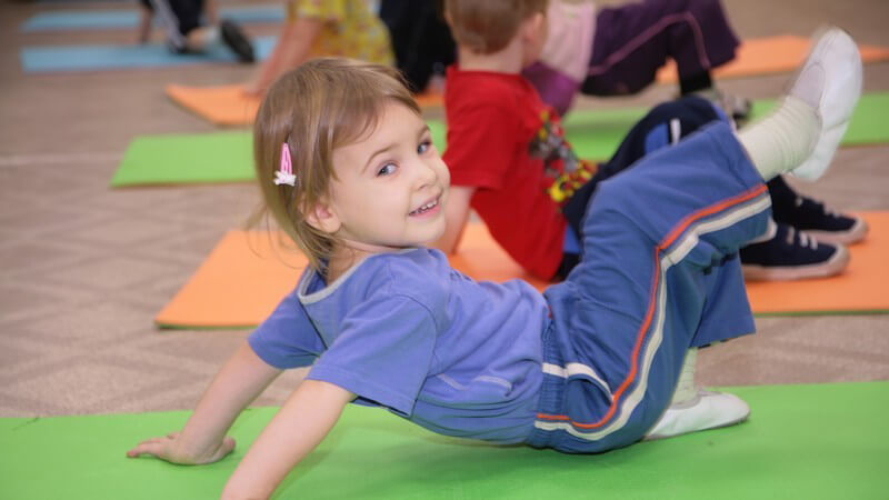 Kleines Mädchen auf Isomatte bei Gymnastikübungen, lächelt in Kamera